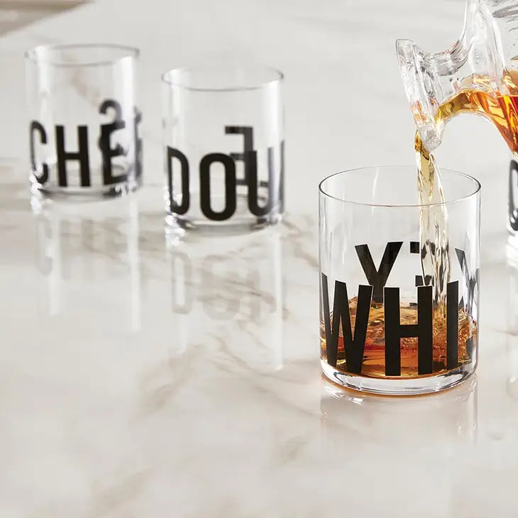 three different styles of double old fashioned glasses with black modern script, lined up on a marble surface while whiskey is being poured