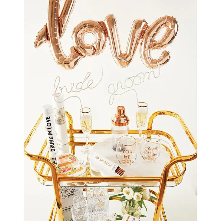 rose gold cocktail shaker displayed on a gold bar cart with champagne glasses and wedding decor