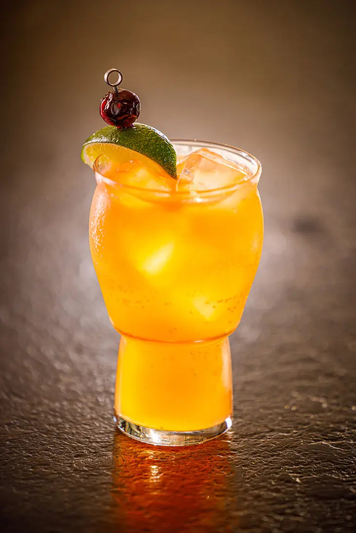 golden cocktail garnished with cherry and lime