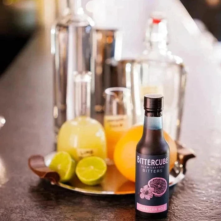 Bottle of Jamaican No.2 Cocktail Bitters by Bittercube displayed with citrus fruits and bottles of spirits in the background 