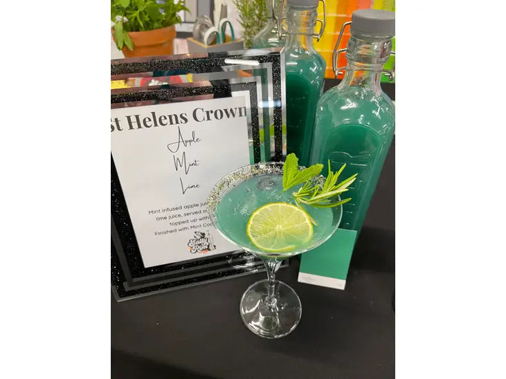 green cocktail in a martini glass rimmed with mint sugar and garnished with a fresh sprig of mint; a store is seen in the background