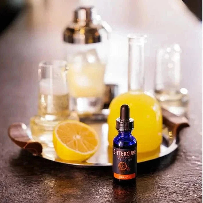 Bittercube bitters bottle on a bar counter with citrus and glasses in the background