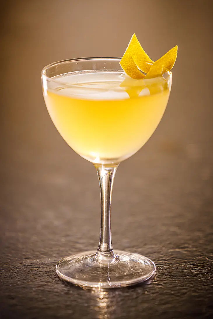 golden cocktail in a martini glass garnished with a cut orange peel