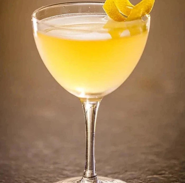 Yellow cocktail in a glass with citrus twist on a brown background