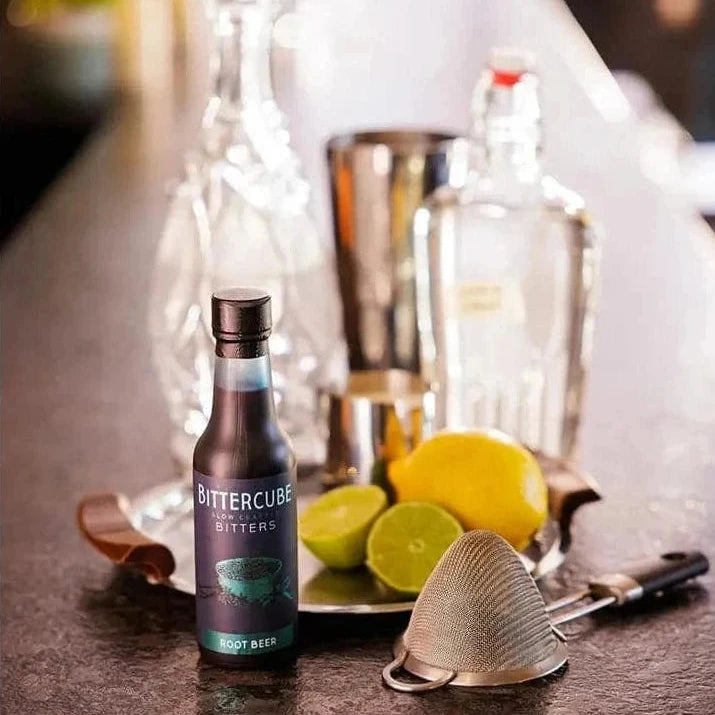 Bottle of Root Beer Cocktail Bitters by Bittercube displayed with citrus and bottles of spirits in the background 