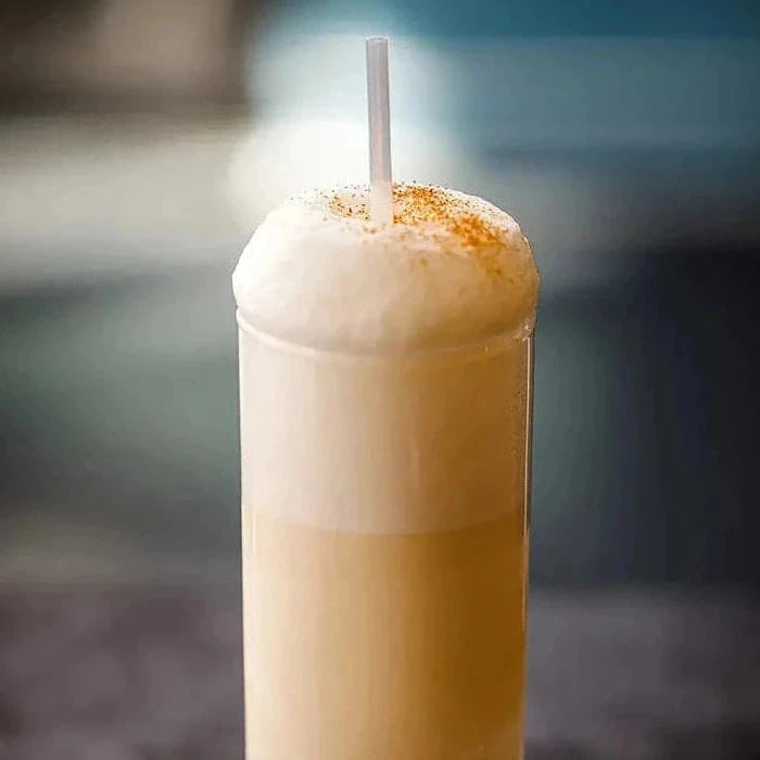 Cream colored drink in a glass with a straw 